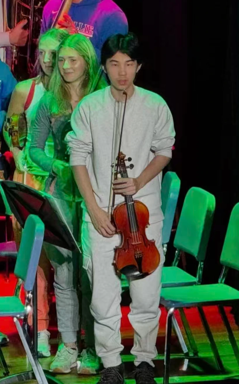 Kevin holding his violin and bow alongside fellow musicians on stage